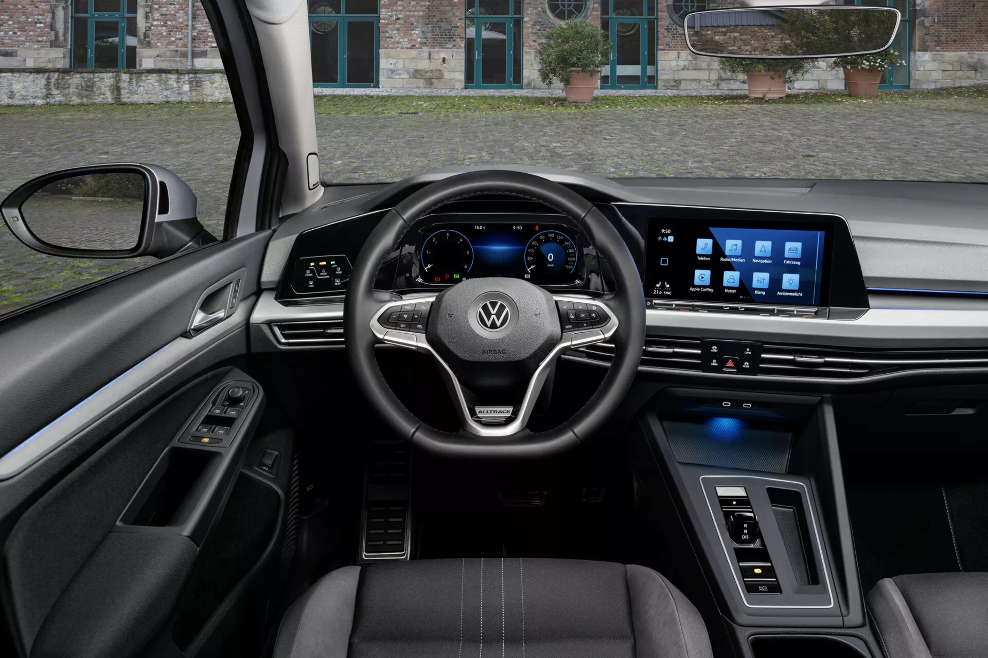 Vista interna del VW Golf Alltrack 2017 dal punto di vista del conducente, mostrando un volante a tre razze con comandi montati e logo Volkswagen, un cruscotto digitale e un ampio sistema di infotainment touchscreen sul cruscotto, evidenziato da funzionalità tecnologiche avanzate, sedili rivestiti in pelle con cuciture a contrasto e una miscela di materiali di lusso e illuminazione ambientale.