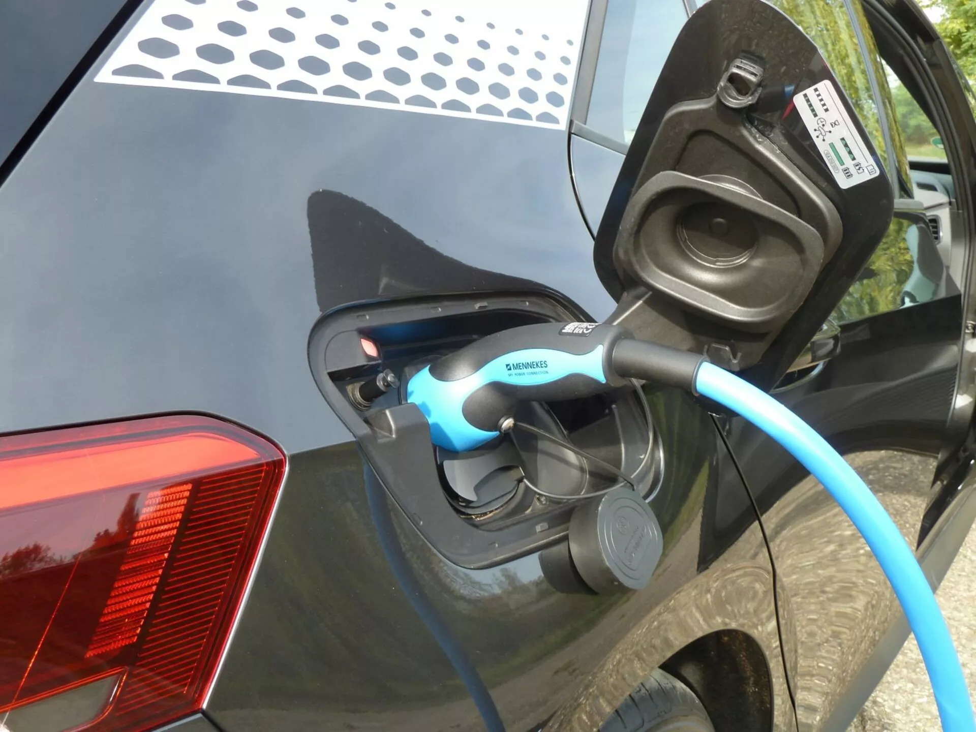 Vista ravvicinata della ricarica di una Volkswagen ID.3 elettrica 2020, concentrandosi sulla porta di carica aperta e sul cavo con marchio Siemens sul pannello posteriore laterale dell'auto, con indicatore LED visibile e dettagli come il design moderno del fanale posteriore LED e la carrozzeria lucida di colore scuro.