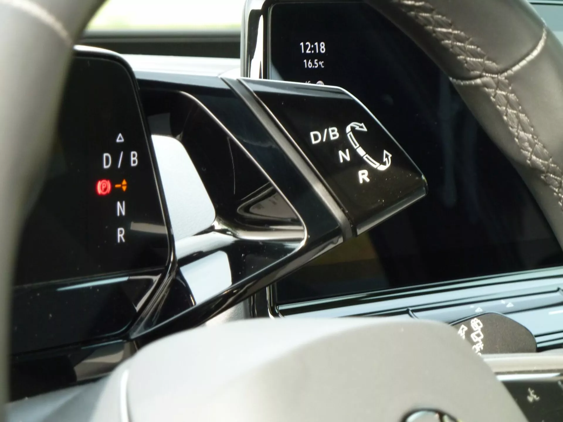 Interno VW ID.3 2020 con vista sulla console centrale e zoom sul selettore del cambio che mostra gli indicatori delle modalità di guida D/B e N/R, orologio digitale alle 12:18 e temperatura a 16,5°, enfatizzando la tecnologia moderna del veicolo e gli elementi di design premium.
