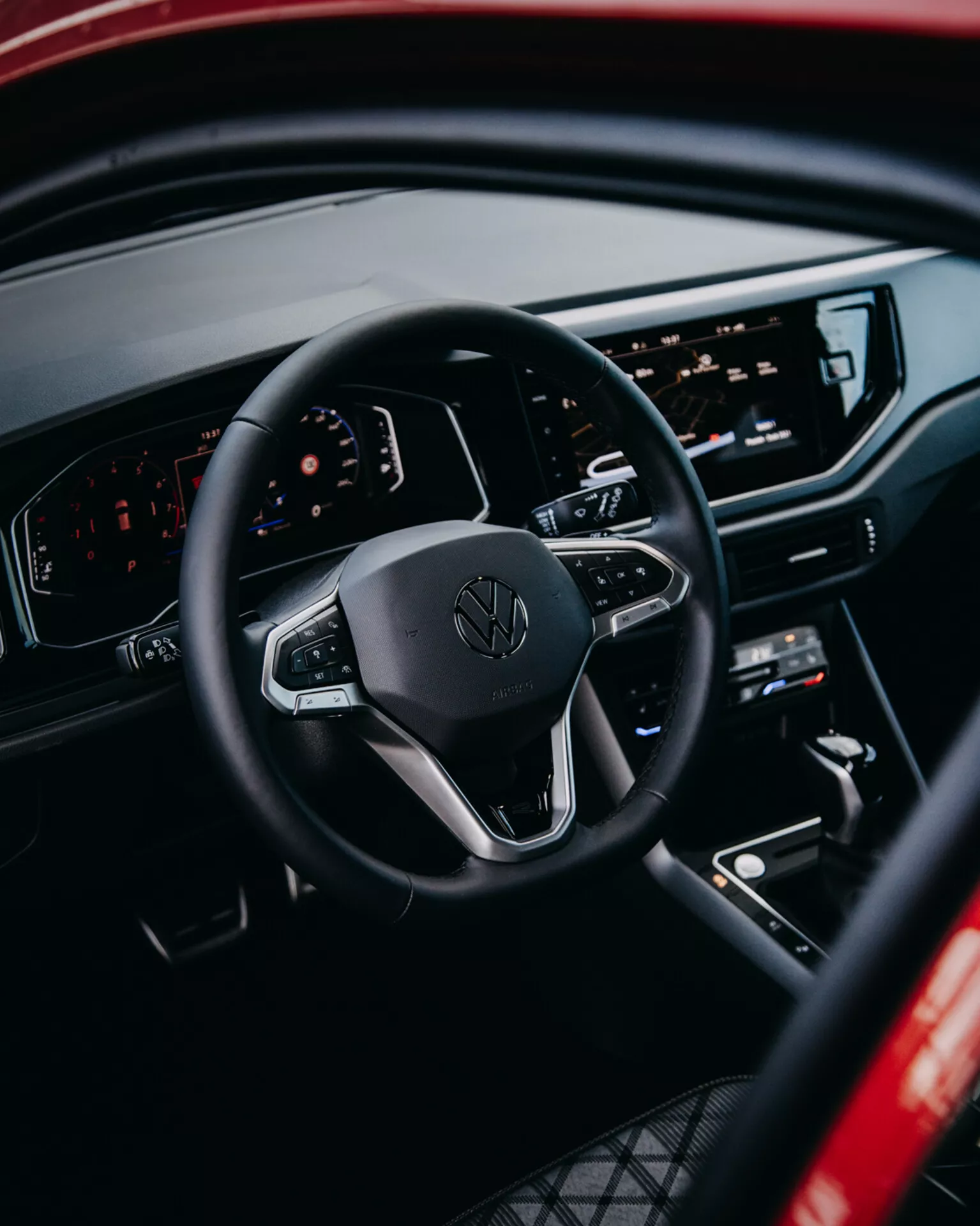 Vista interna della Volkswagen Taigo 2021 evidenziando il volante con comandi, cruscotto digitale e console centrale infotainment dalla prospettiva di un passeggero posteriore